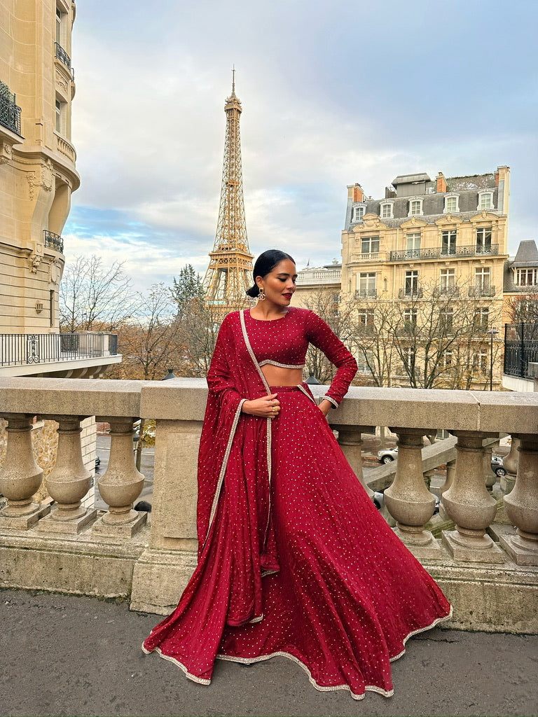 Influencer Alpa Rama wearing a burgundy Dee Kapadiya Honeymoon Lehenga in front of the Eiffel Tower in Paris, blending Indian craftsmanship with romantic elegance.
