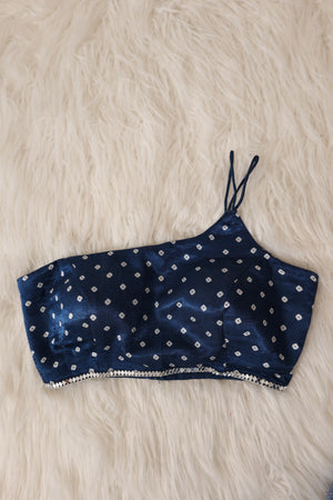 A navy blue satin crop top with white bandhani and a real mirror hem, laid flat on a white faux fur background.
