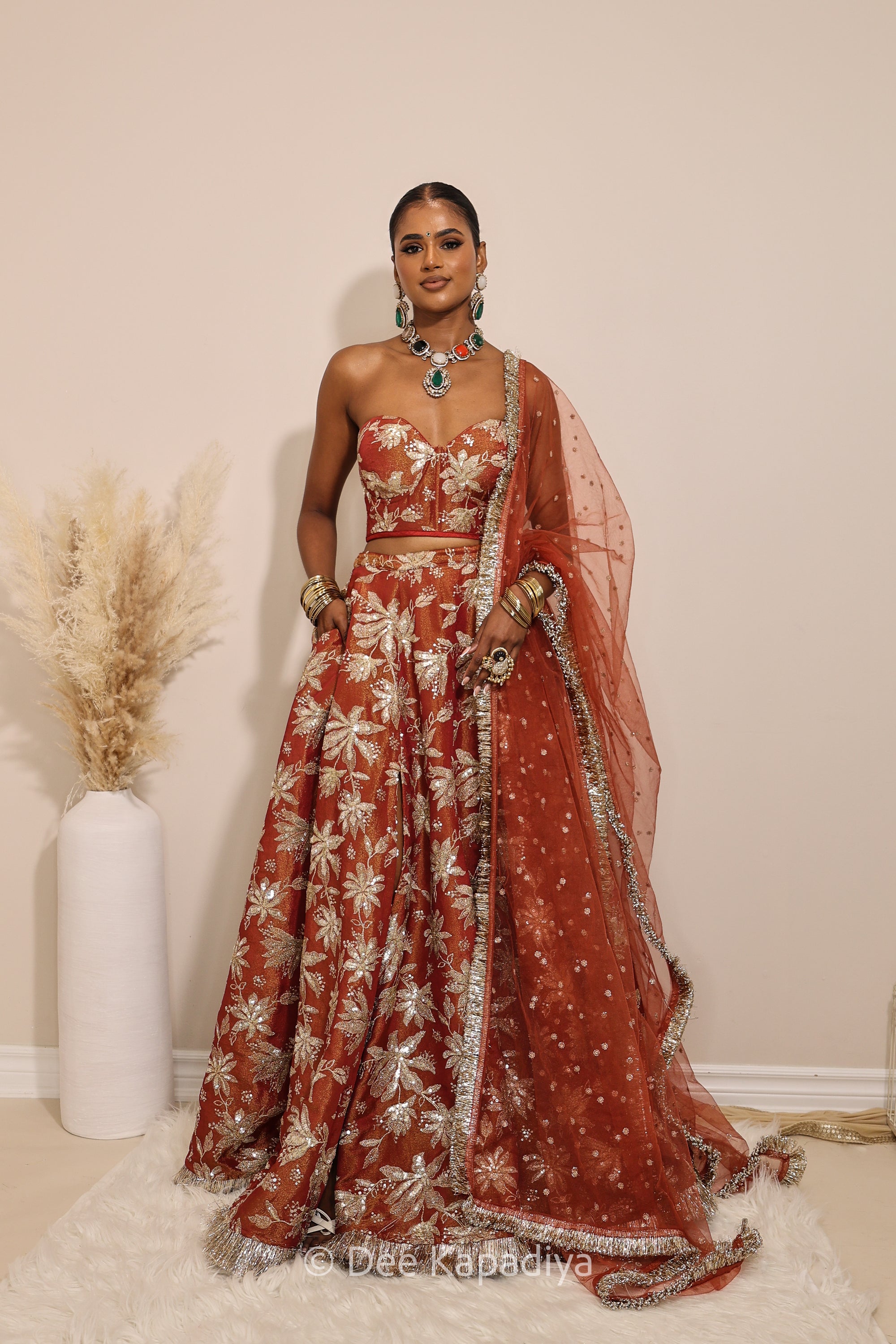 Woman in a red floral dress with a matching dupatta standing against a neutral background. Ahilya Corset with jodha full circle lehenga  front in sunkissed rust for jaggo, mehendi, sangeet fall colours, mehendi, bridal, wedding 