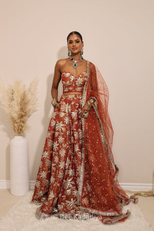 Woman in a red floral dress with a matching dupatta standing against a neutral background. Ahilya Corset with jodha full circle lehenga  front in sunkissed rust for jaggo, mehendi, sangeet fall colours, mehendi, bridal, wedding 
