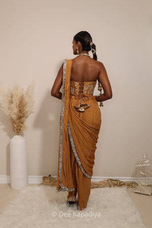 Woman in a floral yellow and gold/silver patterns traditional dhoti saree outfit with jewelry, standing against a plain background. Ahilya corset top with Devi Dhoti saree front in amber sienna mustard yellow for wedding, bridal haldi, mehendi jaggo, sangeet indian wedding events 
