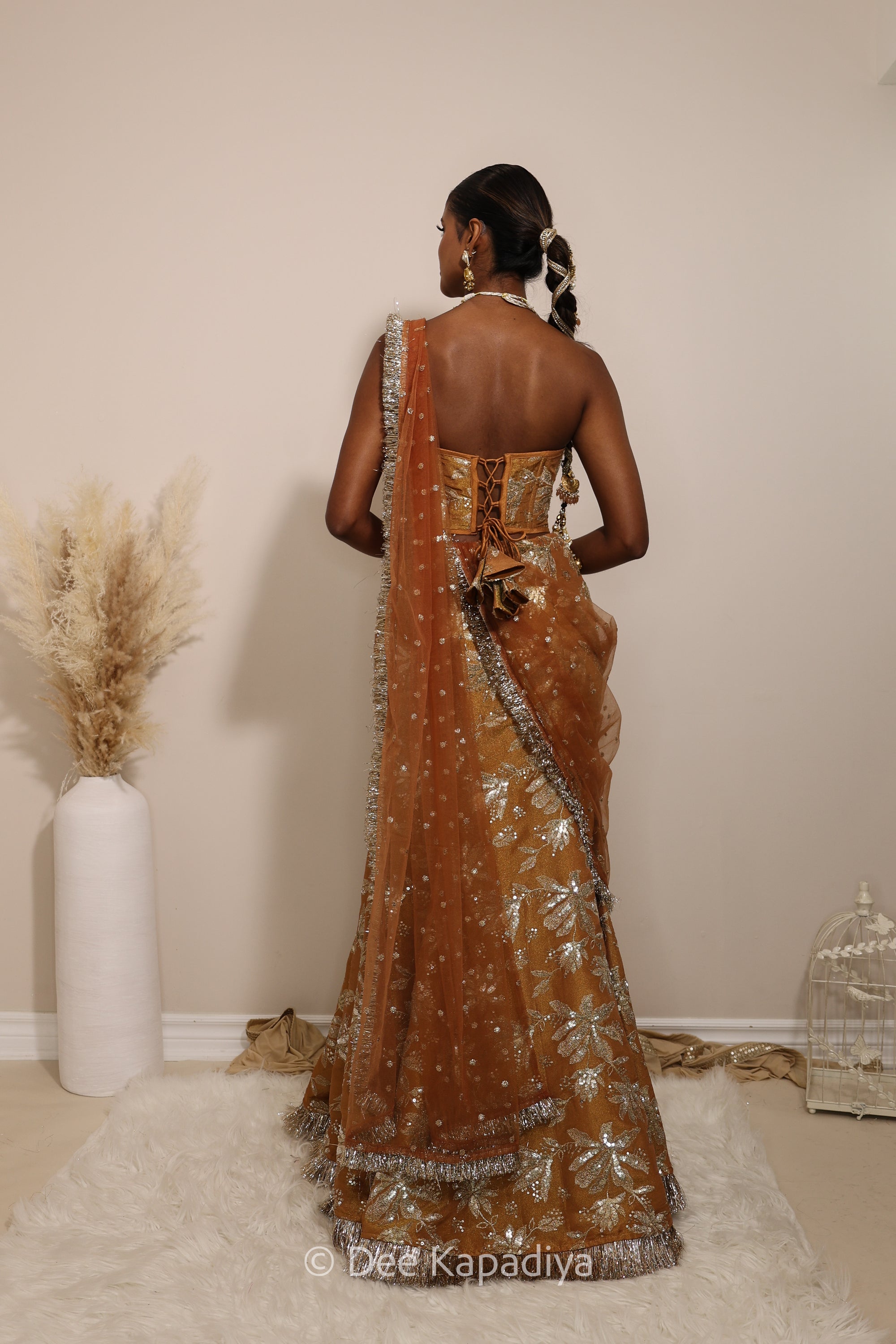 Woman in a floral mustard yellow and gold/silver patterns traditional mermaid lehenga outfit with jewelry, with a sheer dupatta standing against a plain background. Ahilya corset top with Vaani marmaid Lehenga back in amber sienna mustard yellow for wedding, bridal haldi, mehendi jaggo, sangeet indian wedding events 