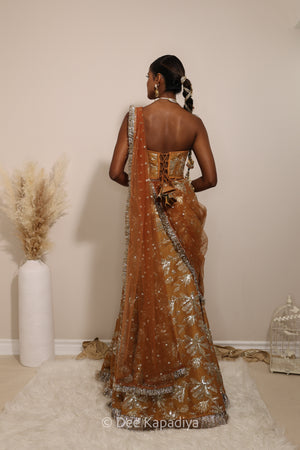 Woman in a floral mustard yellow and gold/silver patterns traditional mermaid lehenga outfit with jewelry, with a sheer dupatta standing against a plain background. Ahilya corset top with Vaani marmaid Lehenga back in amber sienna mustard yellow for wedding, bridal haldi, mehendi jaggo, sangeet indian wedding events 