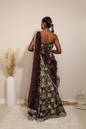 Woman in a floral brown and gold traditional mermaid lehenga outfit with jewelry, with a sheer dupatta standing against a plain background. Ahilya corset top with Vaani marmaid Lehenga back in espresso plum chocolate brown for wedding, bridal haldi, mehendi jaggo, sangeet indian wedding events 