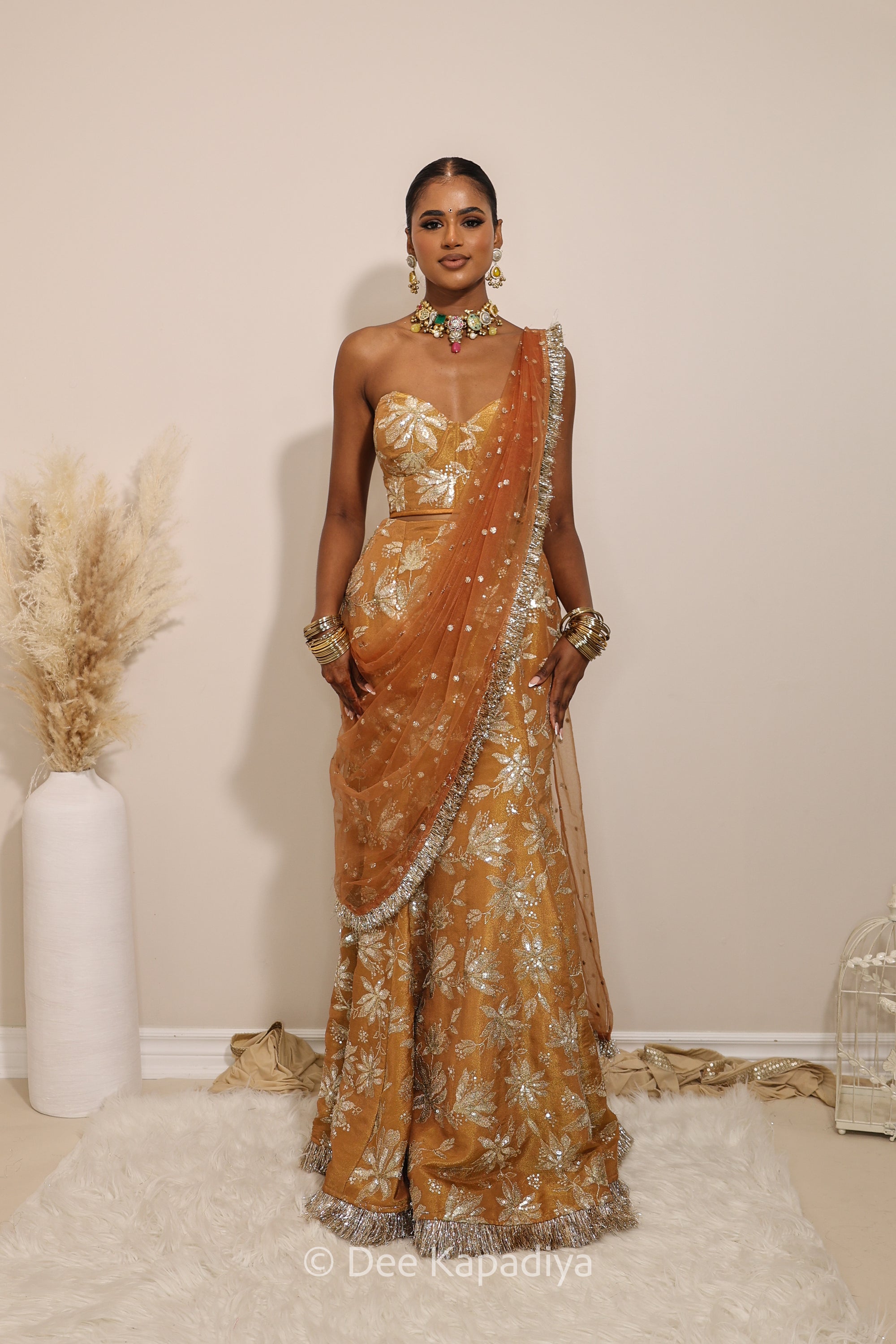 Woman in a floral yellow and gold/silver patterns traditional mermaid lehenga outfit with jewelry, with a sheer dupatta standing against a plain background. Ahilya corset top with Vaani marmaid Lehenga front in amber sienna mustard yellow for wedding, bridal haldi, mehendi jaggo, sangeet indian wedding events 