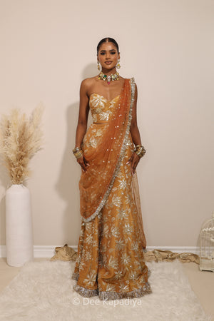Woman in a floral yellow and gold/silver patterns traditional mermaid lehenga outfit with jewelry, with a sheer dupatta standing against a plain background. Ahilya corset top with Vaani marmaid Lehenga front in amber sienna mustard yellow for wedding, bridal haldi, mehendi jaggo, sangeet indian wedding events 