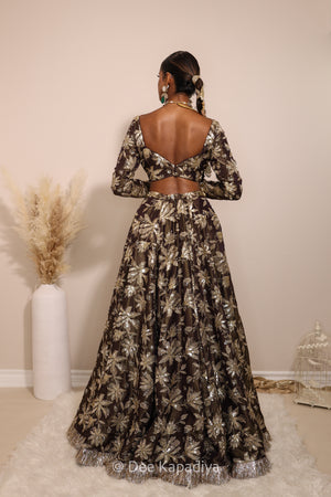 Woman in a floral lehenga skirt with a sheer dupatta standing against a neutral background. Lakshmi top with Jodha Lehenga back in espresso plum chocolate brown for haldi, mehendi jaggo, sangeet indian pre-wedding events