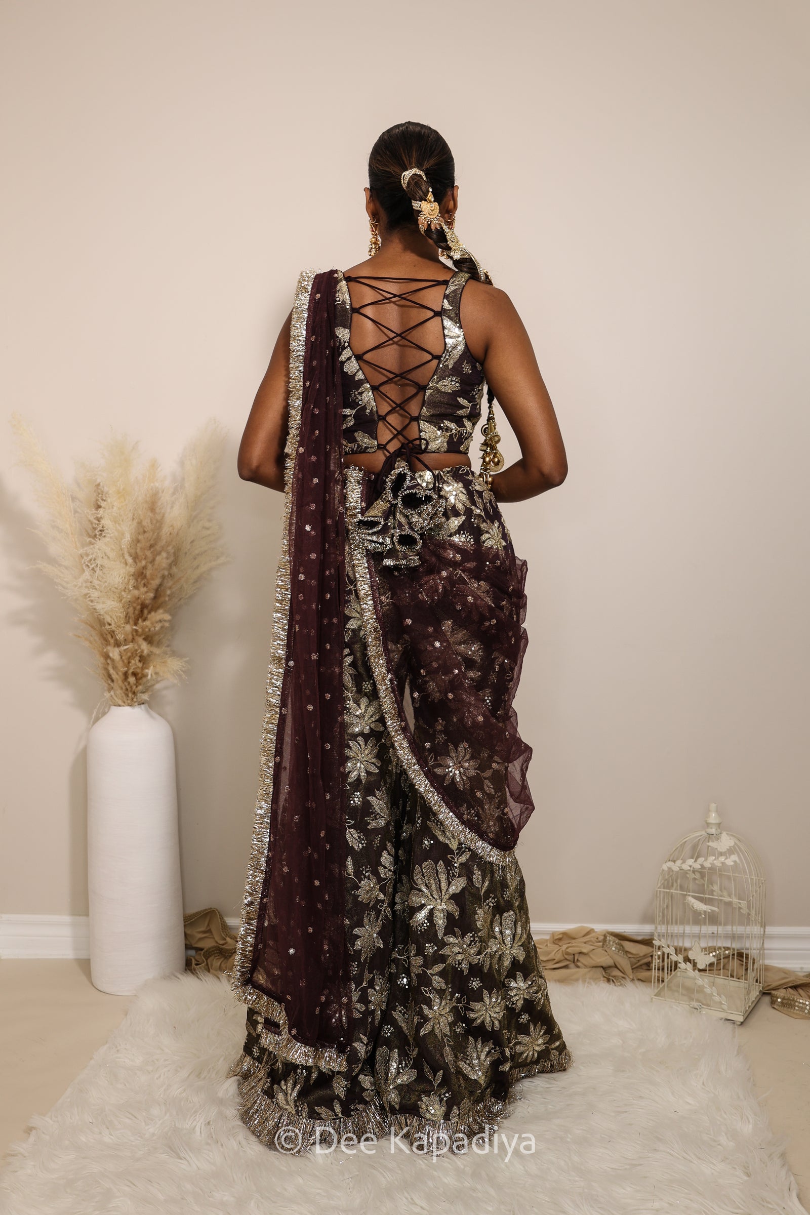 Woman in a floral gharara pants with a sheer dupatta standing against a neutral background. Mehr top with Nur gharara front in espresso plum chocolate brown for haldi, mehendi jaggo, sangeet pre-wedding events