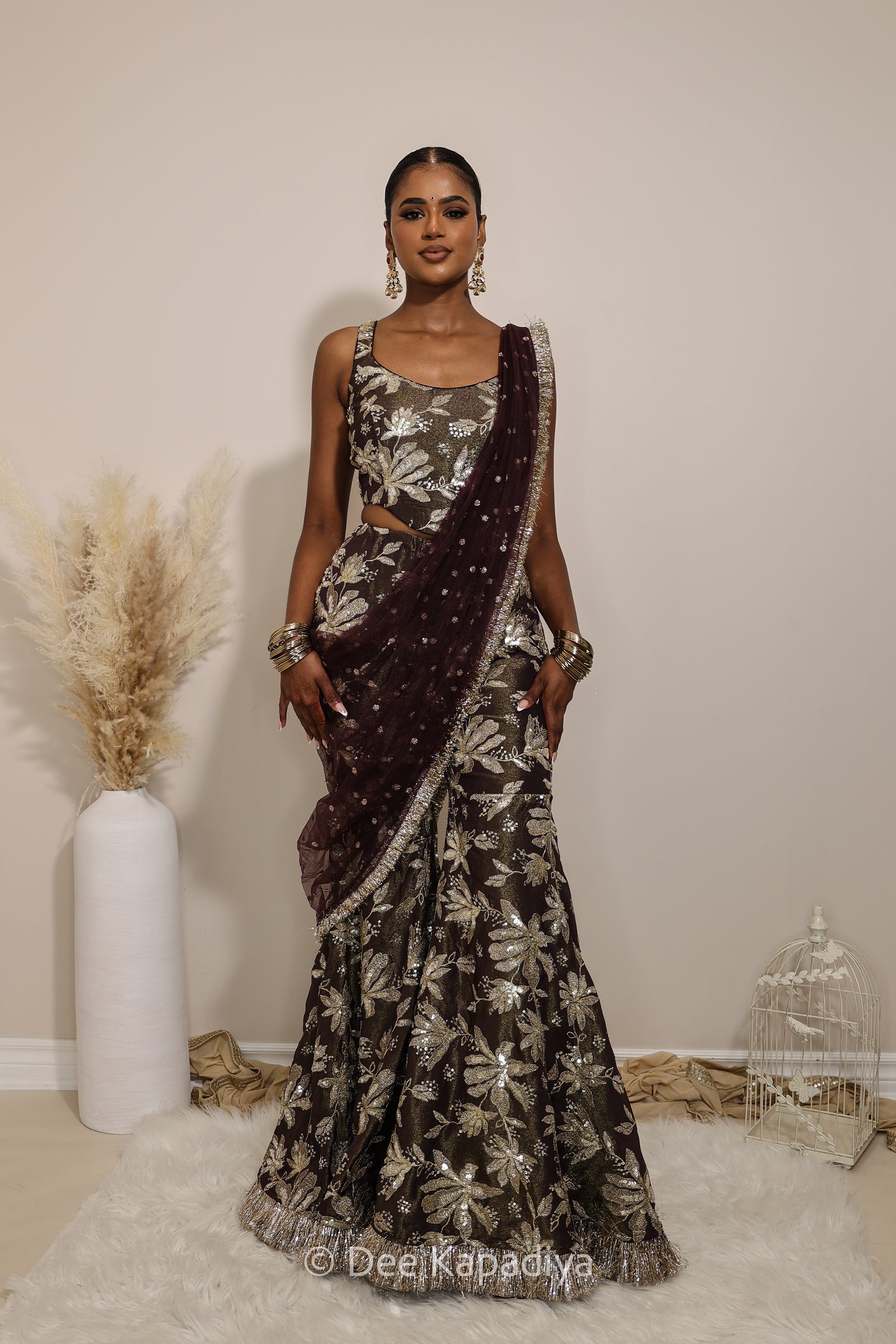 Woman in a floral gharara pants with a sheer dupatta standing against a neutral background. Mehr top with Nur gharara front in espresso plum chocolate brown for haldi, mehendi jaggo, sangeet pre-wedding events