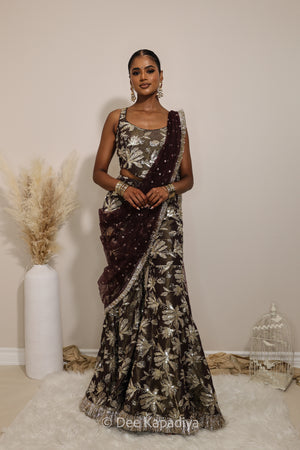 Woman in a floral brown gharara pant with gold patterns with a sheer dupatta standing against a neutral background. Mehr top with Vaani Lehenga front in espresson plum chocolate brown for wedding, bridal haldi, mehendi jaggo, sangeet indian wedding events