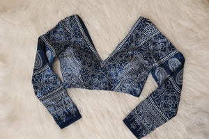 A long-sleeve V-neck blouse with an intricate navy blue and white ajrakh pattern, laid flat on a white faux fur background.