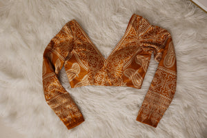 A rust-orange haldi yellow and beige ivory ajrakh printed long-sleeve blouse laid flat on a white faux fur surface.