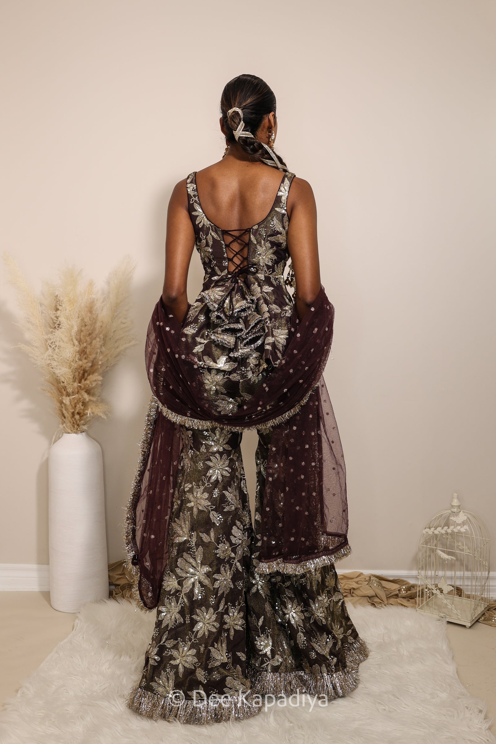 Woman in a floral gharara pants with a sheer dupatta standing against a neutral background. Nur peplum top with Nur gharara front in espresso plum chocolate brown for haldi, mehendi jaggo, sangeet 