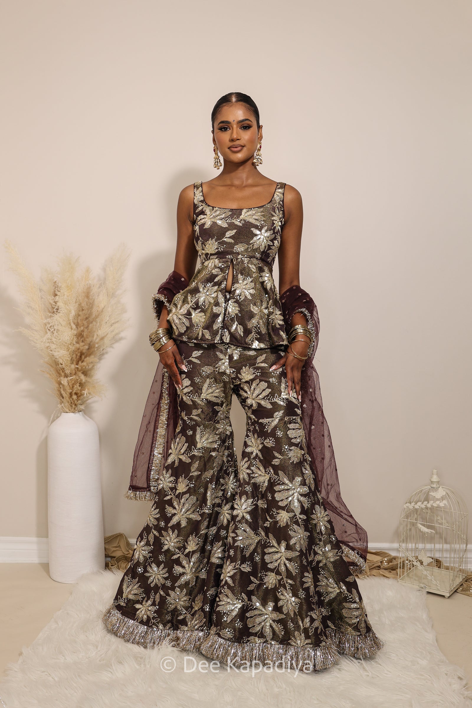 Woman in a floral gharara pants with a sheer dupatta standing against a neutral background. Nur peplum top with Nur gharara front in espresso plum chocolate brown for haldi, mehendi jaggo, sangeet 