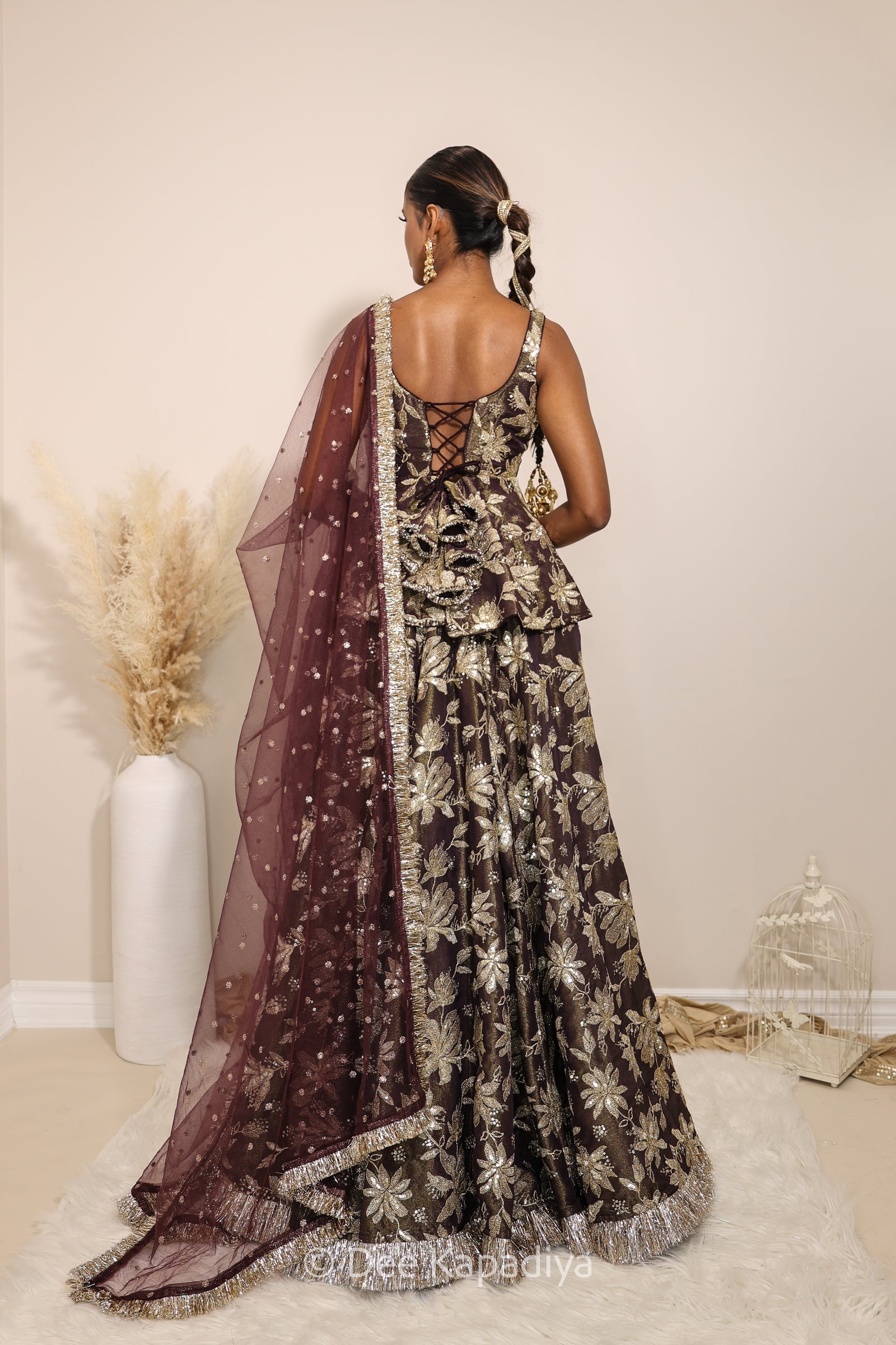 Woman in a floral dress with a sheer dupatta standing against a neutral background. Nur peplum top with jodha full circle lehenga front in espresso plum chocolate brown for haldi, mehendi jaggo, sangeet women wearing lehenga with dupatta