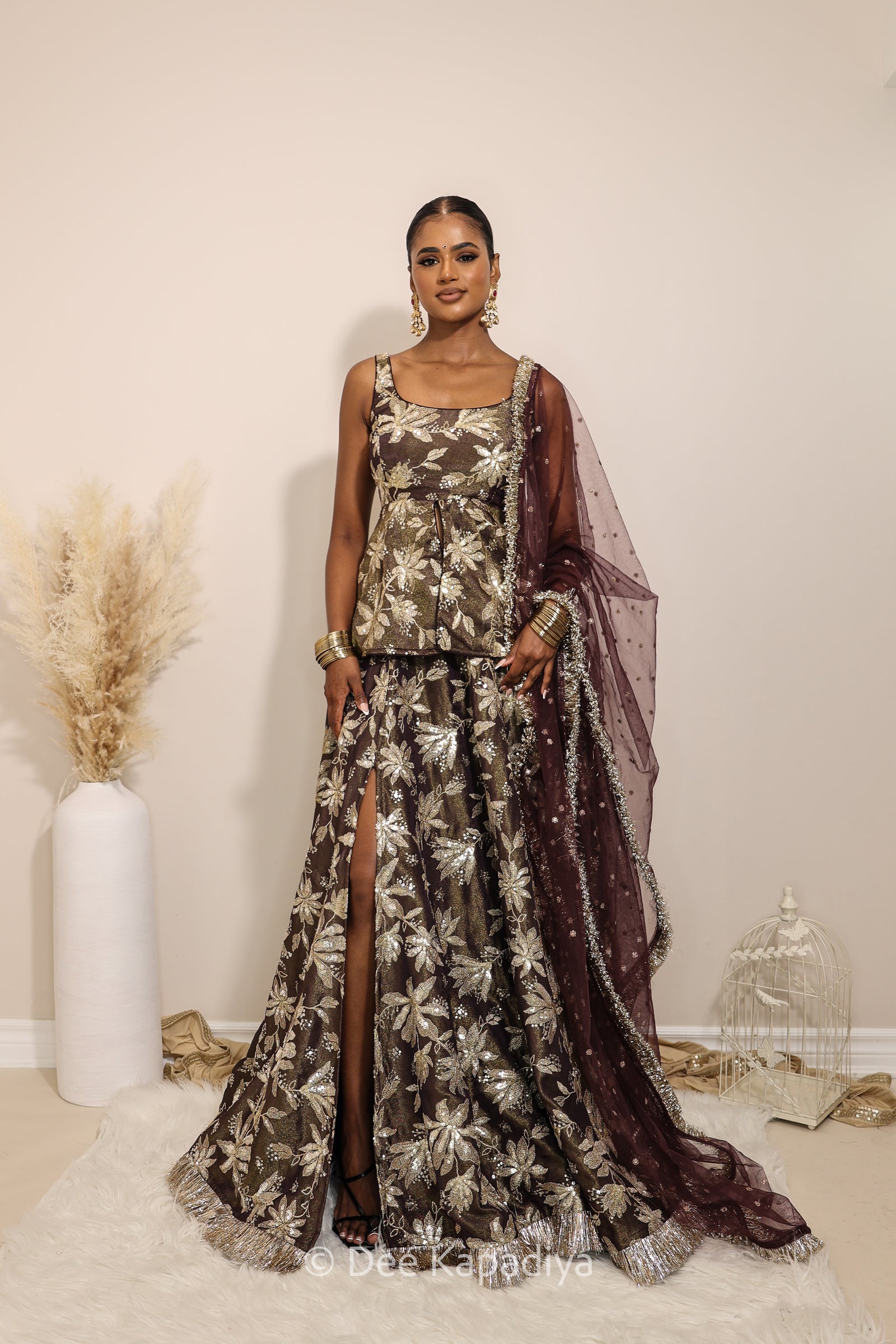 Woman in a floral dress with a sheer dupatta standing against a neutral background. Nur peplum top with jodha full circle lehenga front in espresso plum chocolate brown for haldi, mehendi jaggo, sangeet women wearing lehenga with dupatta
