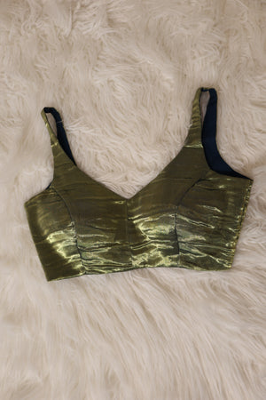 A Indian metallic tissue olive green bralette croptop with a crinkled texture and dark navy blue underwire, laid flat on a white faux fur background.
