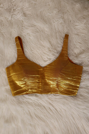A metallic gold bralette croptop with a crinkled, textured finish, laid flat on a white faux fur background.