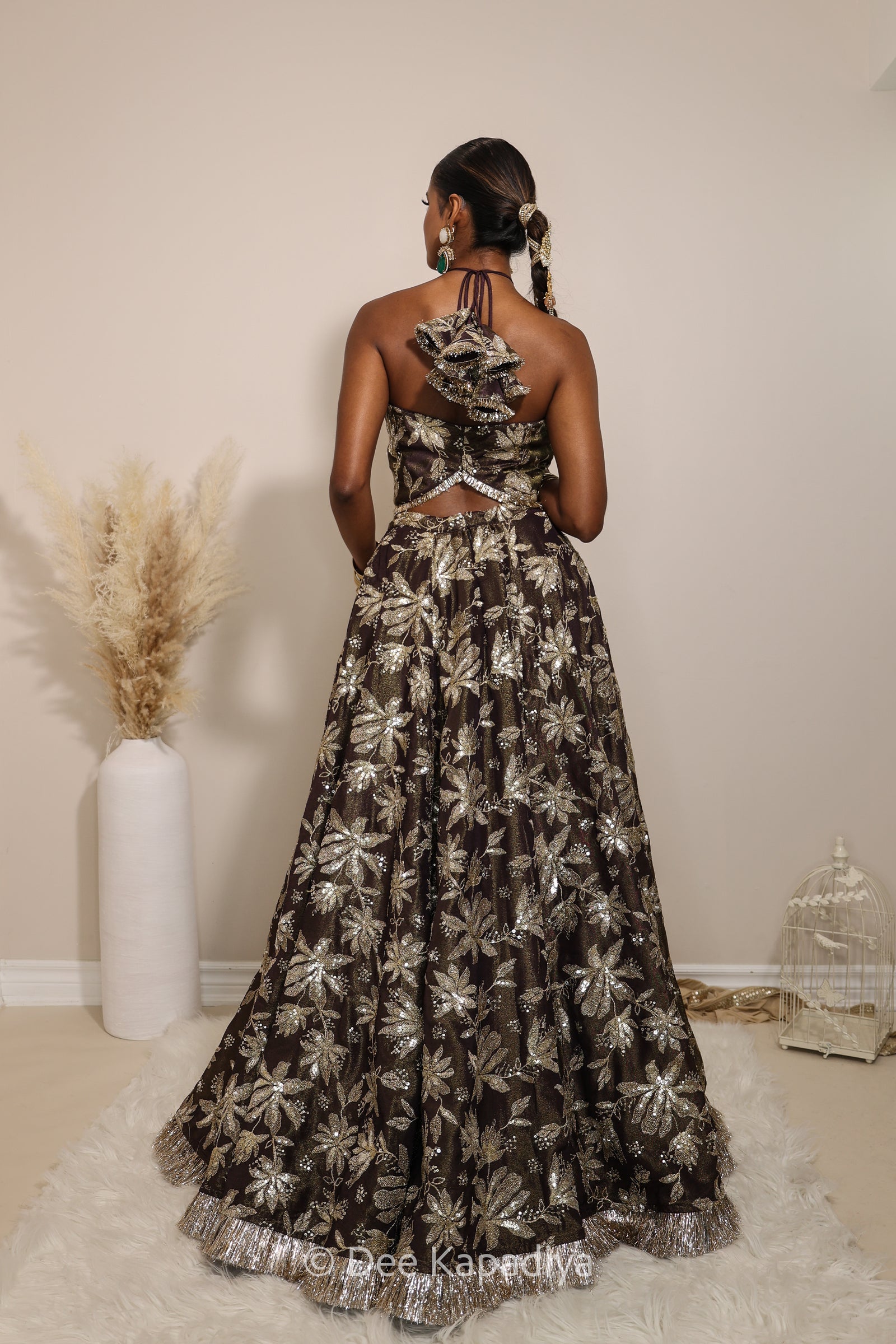 Woman in a floral brown classic lehenga with gold patterns with a sheer dupatta standing against a neutral background. Vaani top with Jodha Lehenga front in espresson plum chocolate brown for wedding, bridal haldi, mehendi jaggo, sangeet indian wedding events