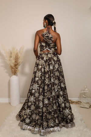 Woman in a floral lehenga skirt with a sheer dupatta standing against a neutral background. Vaani croptop with Jodha lehenga back in espresso plum chocolate brown for haldi, mehendi jaggo, sangeet 