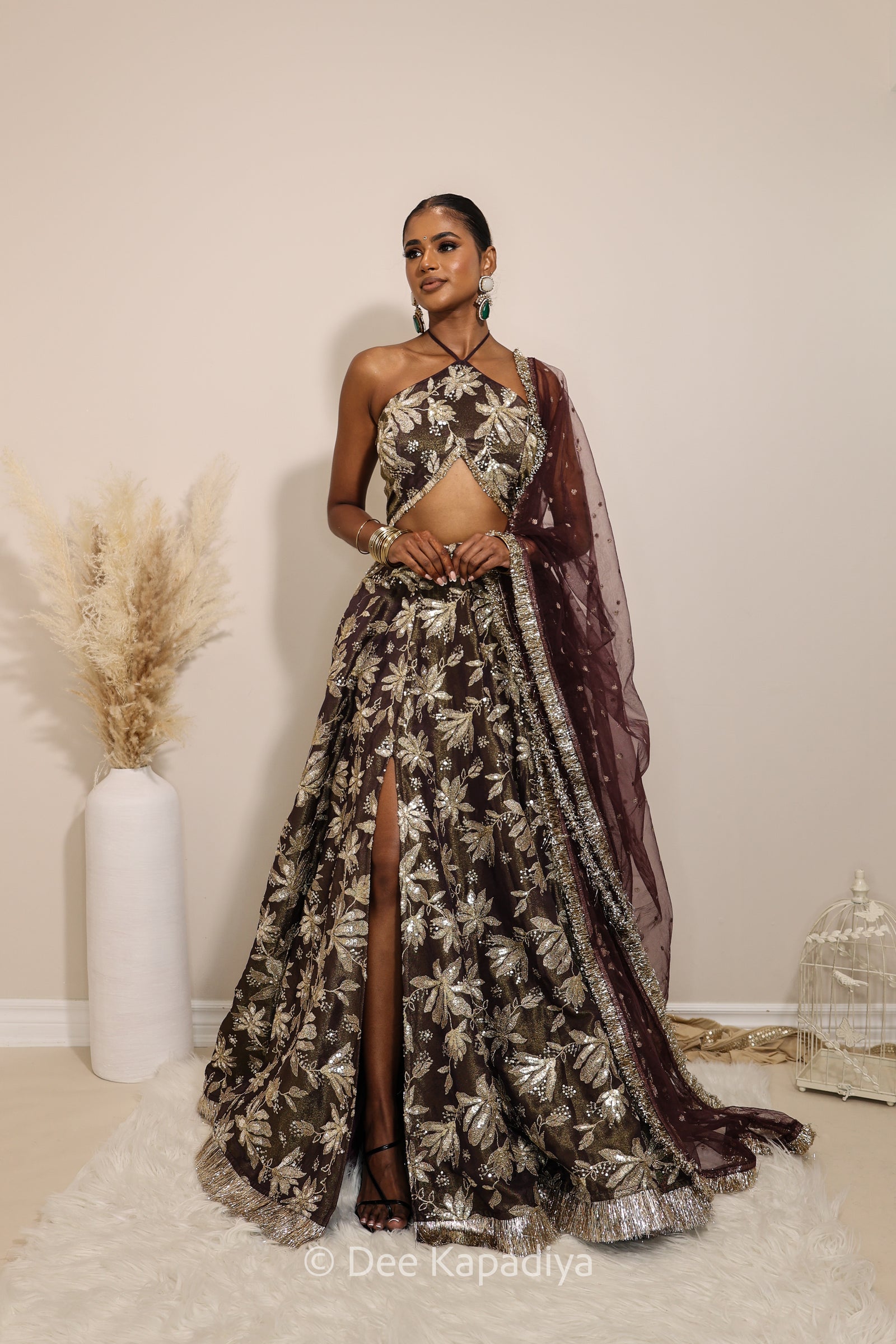 Woman in a floral brown classic lehenga with gold patterns with a sheer dupatta standing against a neutral background. Vaani top with Jodha Lehenga front in espresson plum chocolate brown for wedding, bridal haldi, mehendi jaggo, sangeet indian wedding events