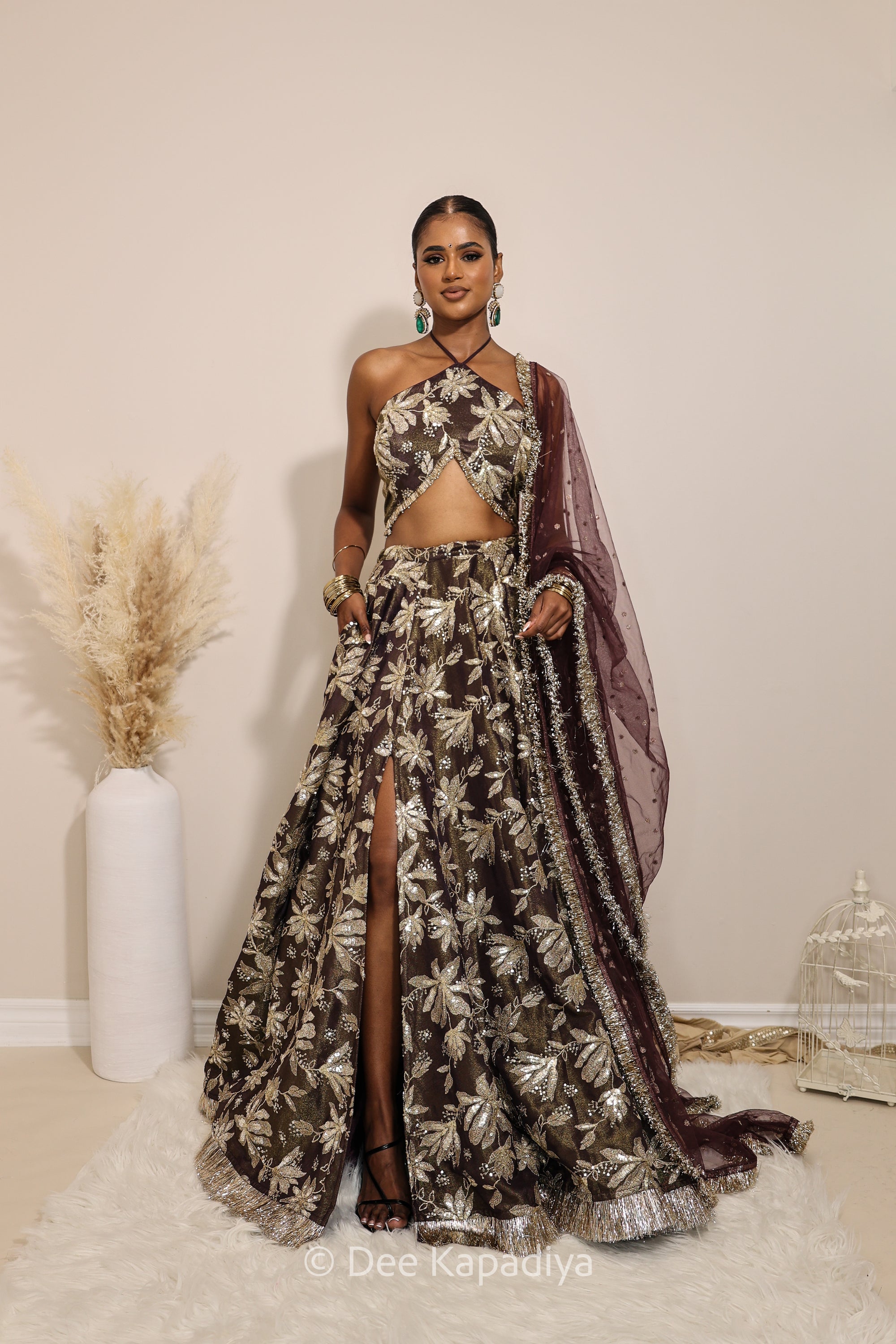 Woman in a floral brown classic lehenga with gold patterns with a sheer dupatta standing against a neutral background. Vaani top with Jodha Lehenga front in espresson plum chocolate brown for wedding, bridal haldi, mehendi jaggo, sangeet indian wedding events