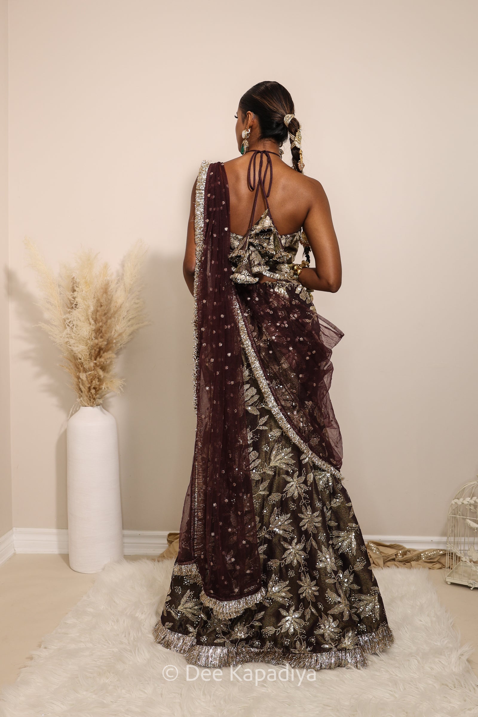 Woman in a floral brown and gold/silver patterns traditional mermaid lehenga outfit with jewelry, with a sheer dupatta standing against a plain background. Vaani top with Vaani marmaid Lehenga front in espresso plum chocolate brown for wedding, bridal haldi, mehendi jaggo, sangeet indian wedding events 