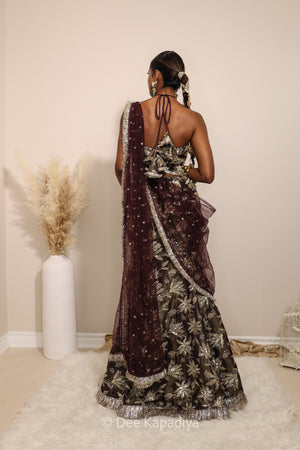 Woman in a floral brown mermaid lehenga with gold patterns with a sheer dupatta standing against a neutral background. Vaani top with Vaani Lehenga back in espresso plum chocolate brown for wedding, bridal haldi, mehendi jaggo, sangeet indian wedding events