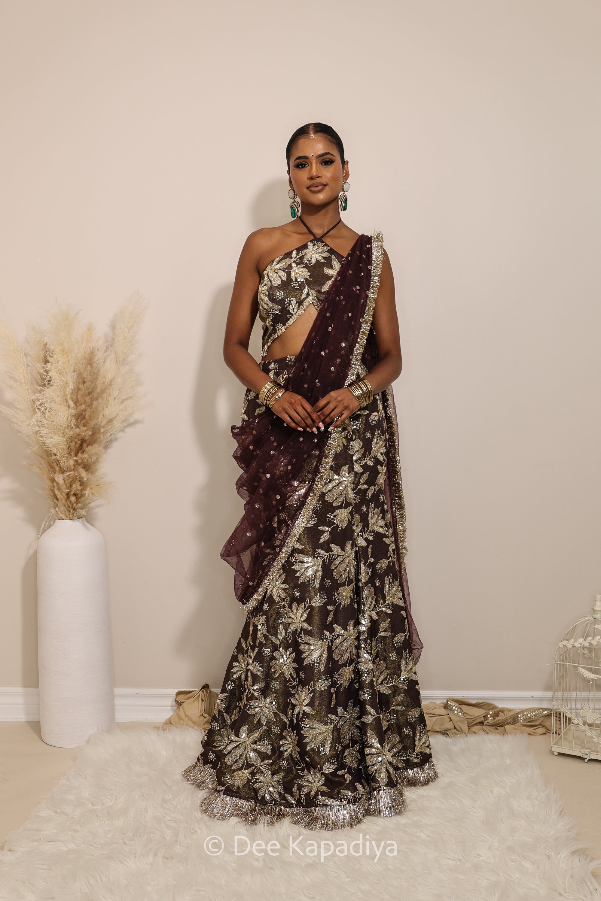 Woman in a floral brown and gold/silver patterns traditional mermaid lehenga outfit with jewelry, with a sheer dupatta standing against a plain background. Vaani top with Vaani marmaid Lehenga front in espresso plum chocolate brown for wedding, bridal haldi, mehendi jaggo, sangeet indian wedding events 
